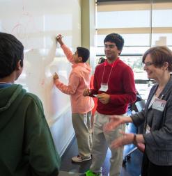 A speaker works with students at a whiteboard.